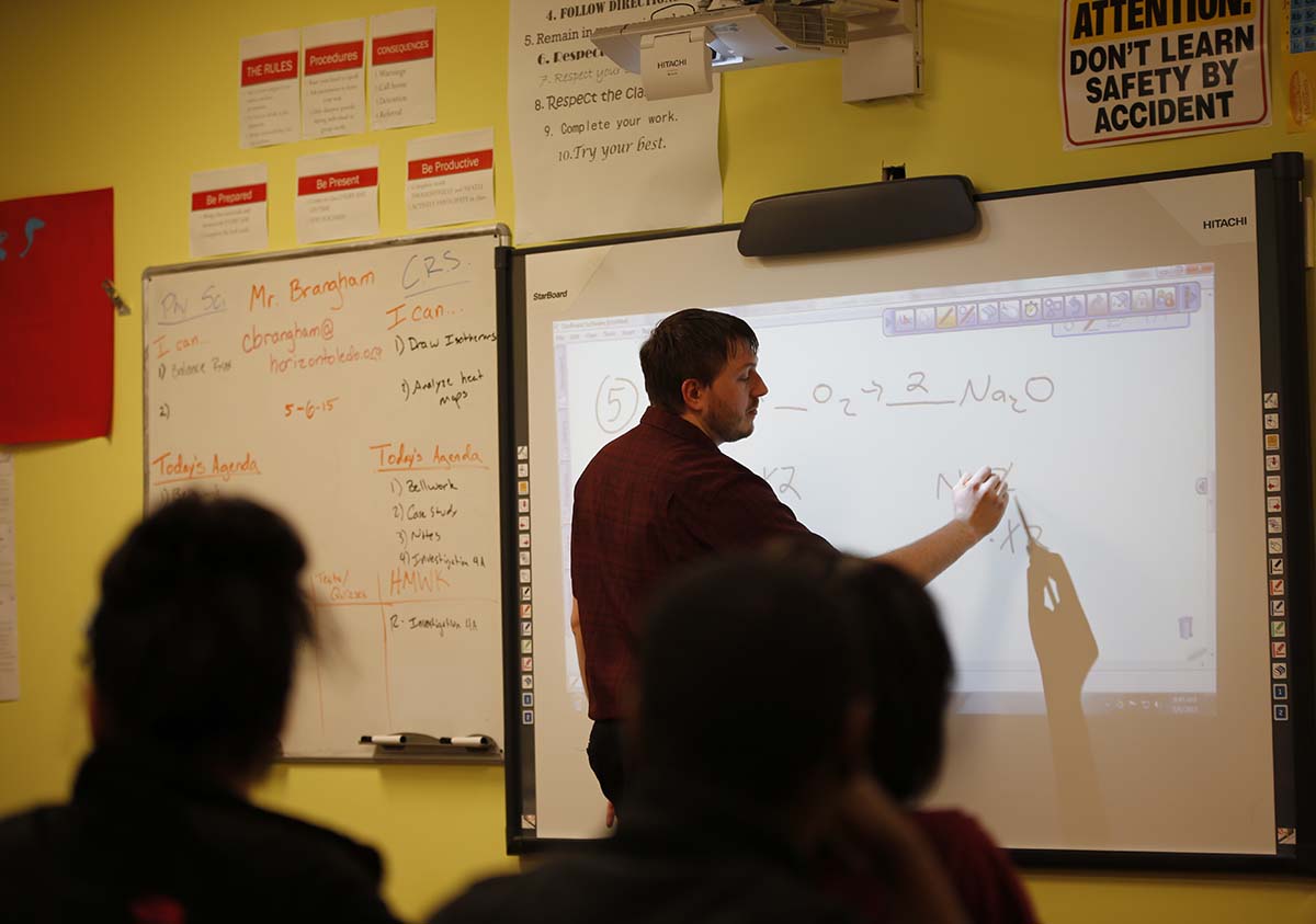 HSA Teacher smiles while kneeling beside a young student in a classroom setting.